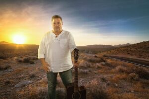 Brian Hughes posing with a guitar in the desert. during sunset.