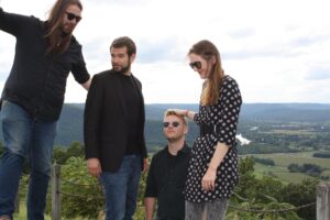 3 males and a female standing on a hill. A photo of the band Telephone Party.