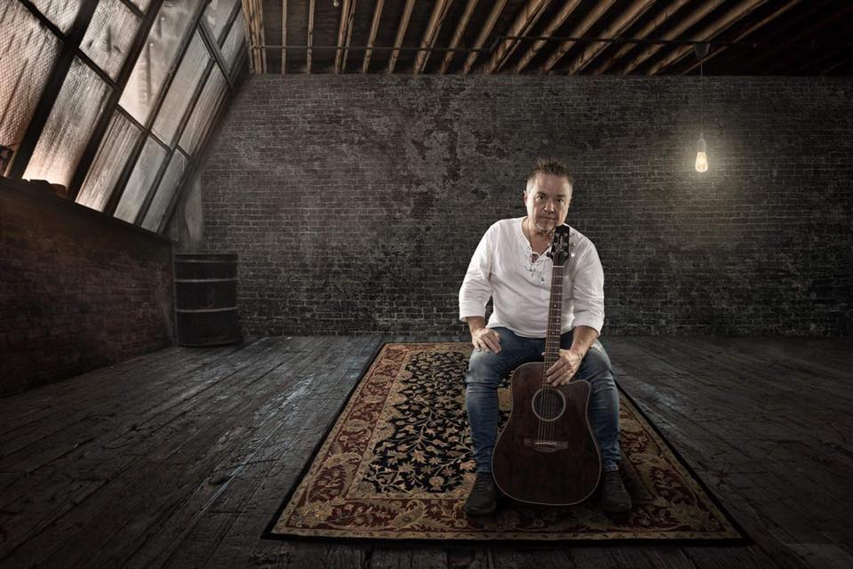 Brian Hughes with a guitar in an empty room.