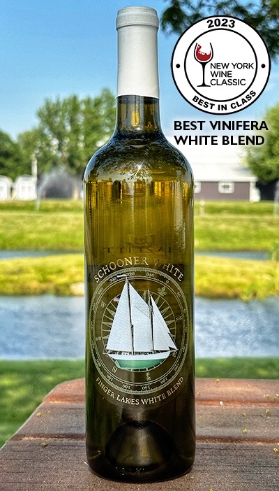 Bottle of Schooner White Finger Lakes Blend on a picnic table with a pond in the background.